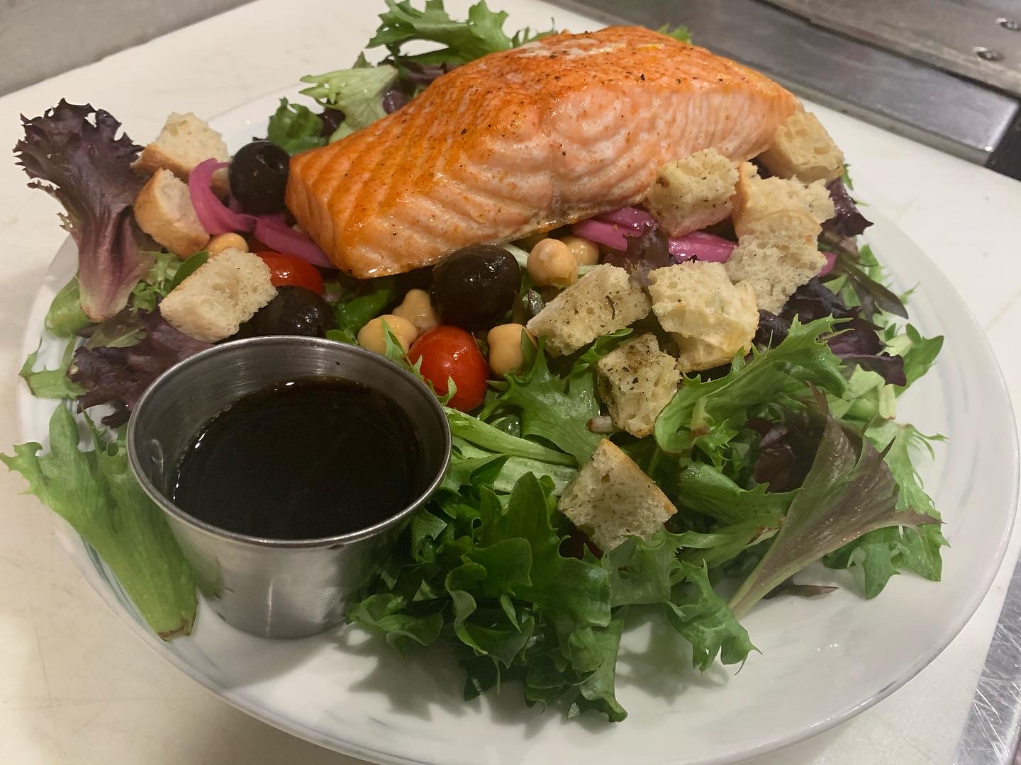 A plated salmon entrée with greens and tomatoes